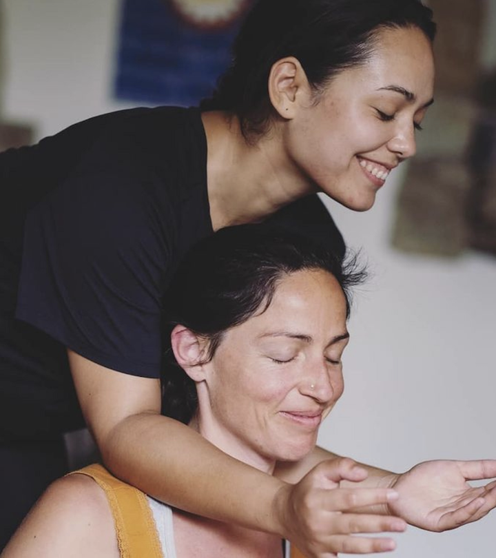 A Thai massage therapist applying pressure to a client's shoulders who is smiling with her eyes closed